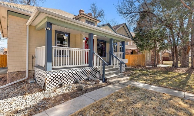 view of front of house with a porch, fence, and a chimney