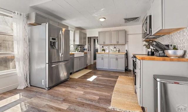 kitchen with visible vents, gray cabinetry, wood counters, tasteful backsplash, and stainless steel appliances