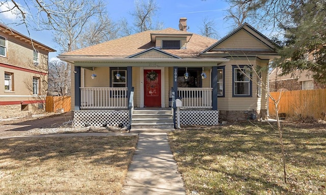 bungalow-style house featuring a front lawn, fence, roof with shingles, covered porch, and a chimney