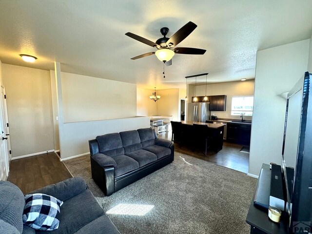 living room featuring ceiling fan with notable chandelier, a textured ceiling, and baseboards