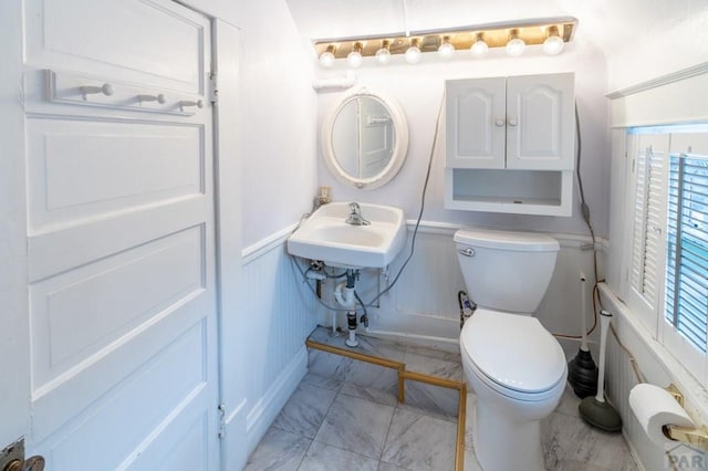 half bath featuring marble finish floor, toilet, and plenty of natural light