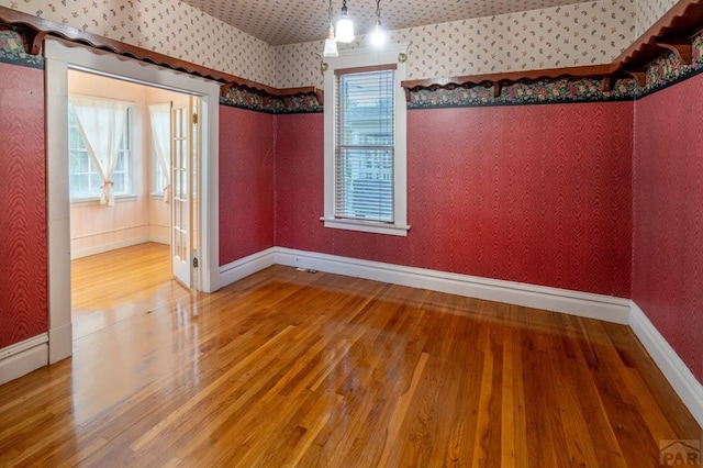 empty room featuring baseboards, wood finished floors, and wallpapered walls