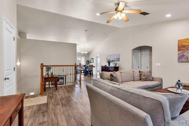 living room featuring wood finished floors, ceiling fan with notable chandelier, arched walkways, lofted ceiling, and recessed lighting