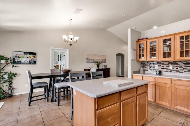 kitchen featuring lofted ceiling, an inviting chandelier, backsplash, light tile patterned floors, and arched walkways