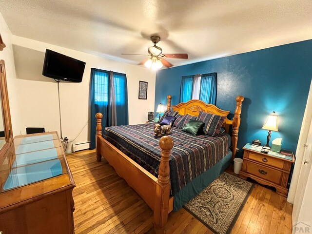 bedroom with a ceiling fan, light wood-style flooring, and baseboard heating