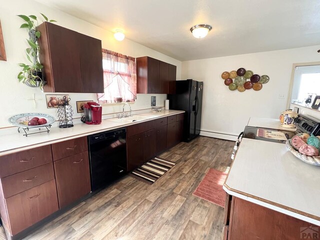 kitchen featuring dark wood-style floors, baseboard heating, light countertops, black appliances, and a sink