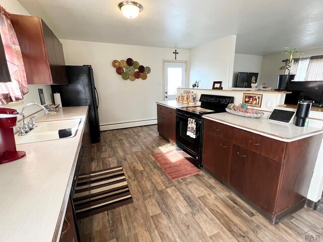 kitchen featuring black electric range oven, wood finished floors, light countertops, a baseboard heating unit, and a sink