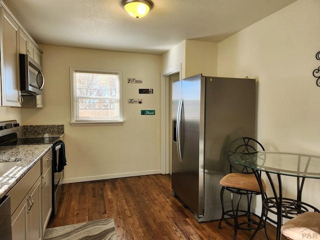 kitchen featuring a textured ceiling, stainless steel appliances, dark wood-style flooring, baseboards, and dark stone countertops