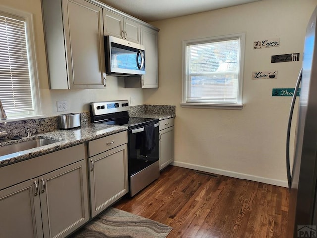 kitchen featuring baseboards, dark wood finished floors, light stone counters, stainless steel appliances, and a sink