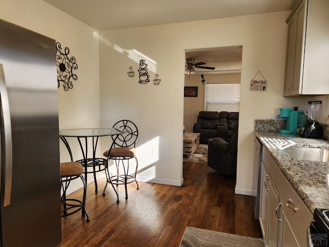 kitchen featuring dark wood finished floors, ceiling fan, open floor plan, freestanding refrigerator, and light stone countertops