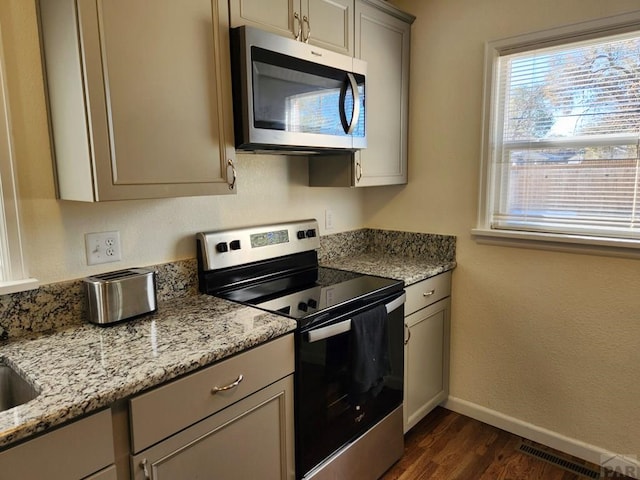 kitchen with appliances with stainless steel finishes, baseboards, dark wood-type flooring, and light stone counters