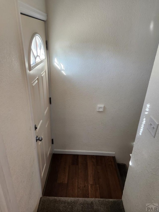 doorway featuring dark wood-style floors, a textured wall, and baseboards