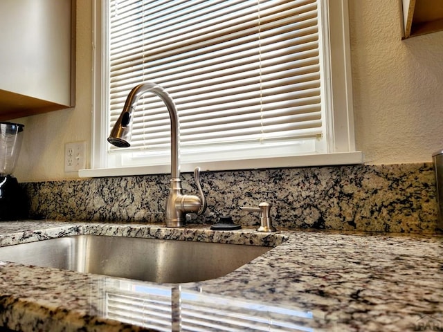 details with a textured wall, a sink, and light stone countertops