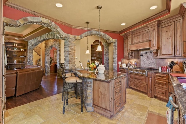 kitchen with arched walkways, stainless steel gas cooktop, a kitchen breakfast bar, hanging light fixtures, and dark stone counters