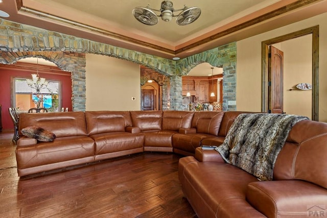 living room with arched walkways, a raised ceiling, wood finished floors, an inviting chandelier, and crown molding