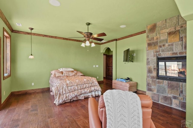 bedroom featuring dark wood-type flooring, arched walkways, a fireplace, and crown molding