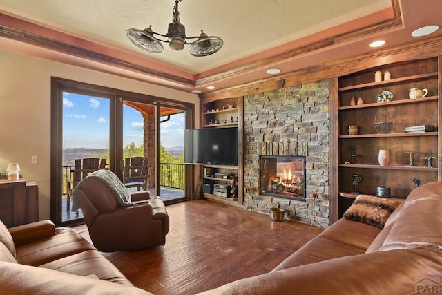 living room with built in shelves, crown molding, a fireplace, a raised ceiling, and wood finished floors