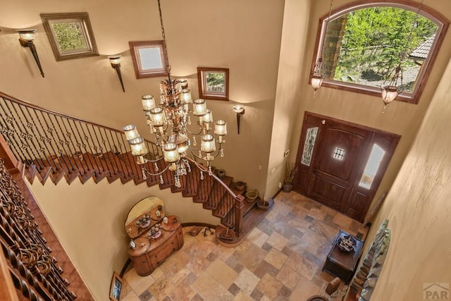 entrance foyer with stone finish flooring, a notable chandelier, stairway, and baseboards