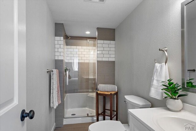 bathroom with a stall shower, visible vents, vanity, and toilet