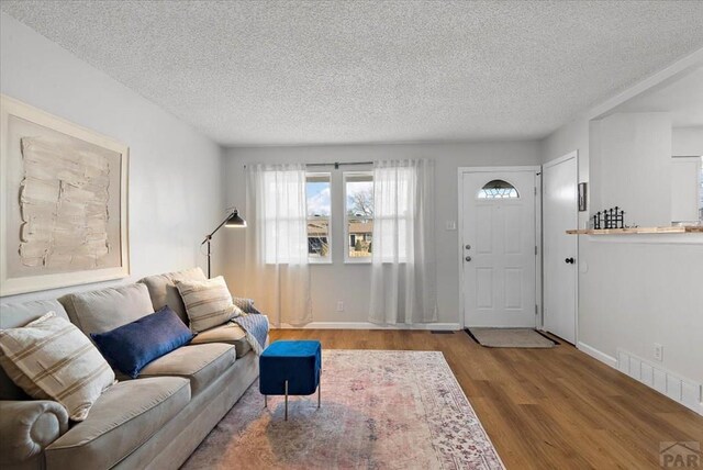 living area featuring a textured ceiling, wood finished floors, visible vents, and baseboards