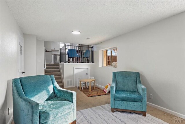 sitting room with a textured ceiling, carpet flooring, visible vents, baseboards, and stairway