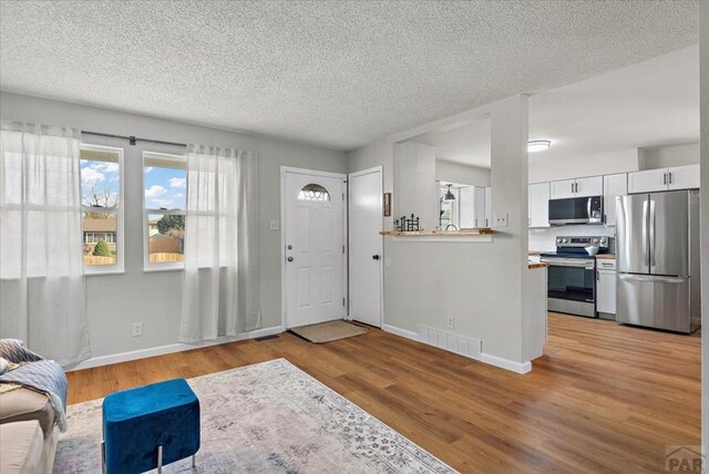 entryway featuring a textured ceiling, light wood finished floors, visible vents, and baseboards