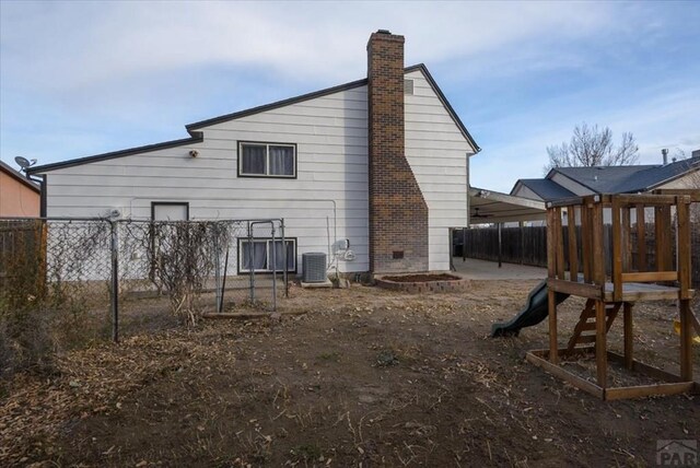 rear view of house featuring a playground, fence, a chimney, and central air condition unit