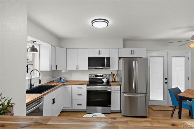 kitchen featuring butcher block counters, appliances with stainless steel finishes, white cabinetry, pendant lighting, and a sink