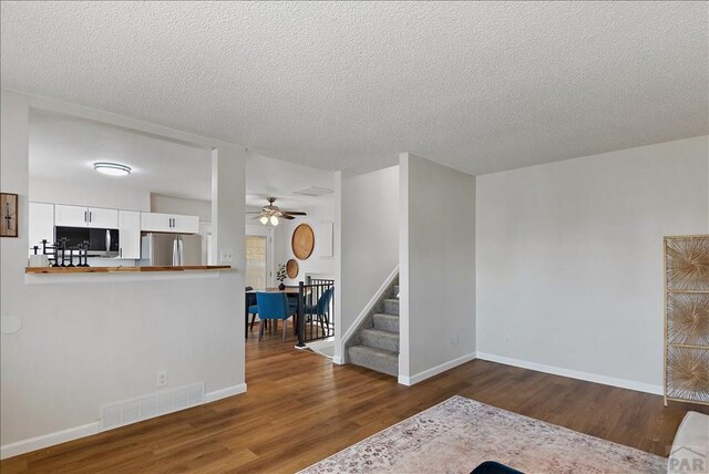 living room featuring visible vents, baseboards, ceiling fan, stairway, and dark wood-type flooring