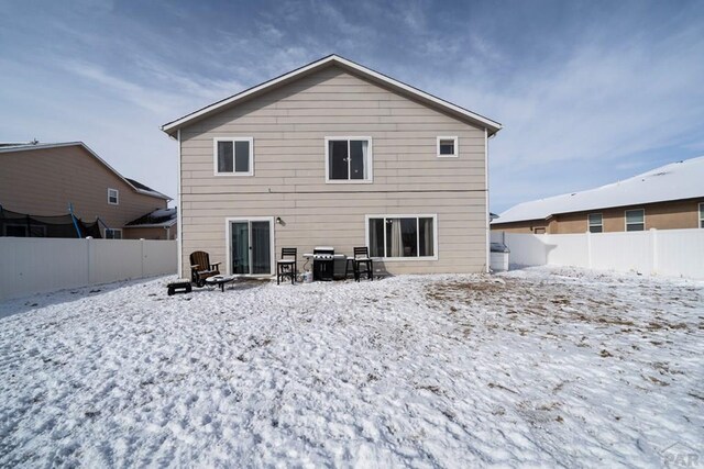 snow covered rear of property featuring a fenced backyard and a fire pit