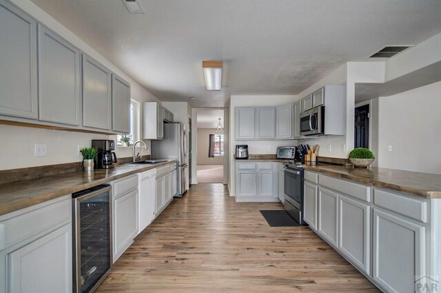 kitchen with wine cooler, stainless steel appliances, dark countertops, visible vents, and a sink