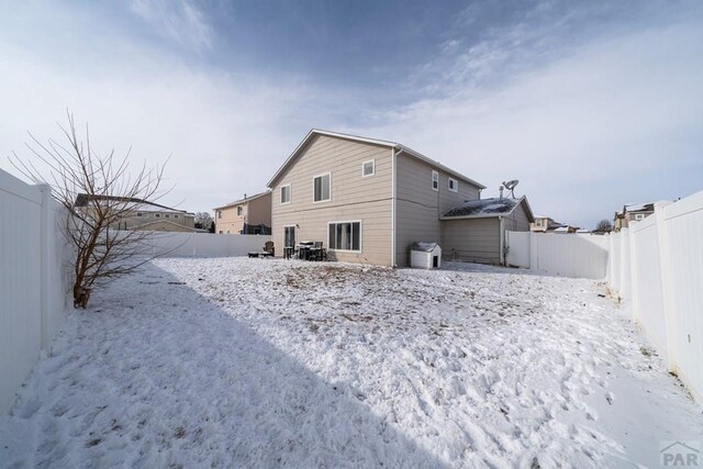 snow covered back of property featuring a fenced backyard