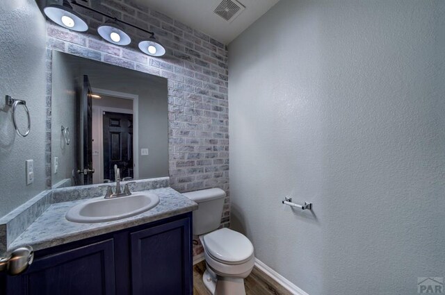 half bath featuring baseboards, visible vents, toilet, wood finished floors, and vanity