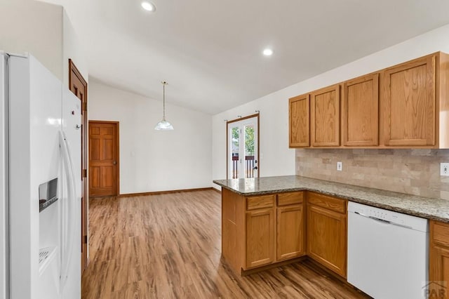 kitchen featuring pendant lighting, vaulted ceiling, wood finished floors, white appliances, and a peninsula