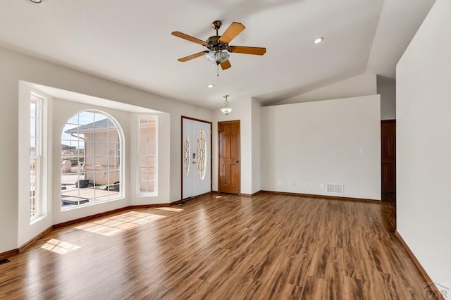 empty room featuring baseboards, visible vents, vaulted ceiling, and wood finished floors