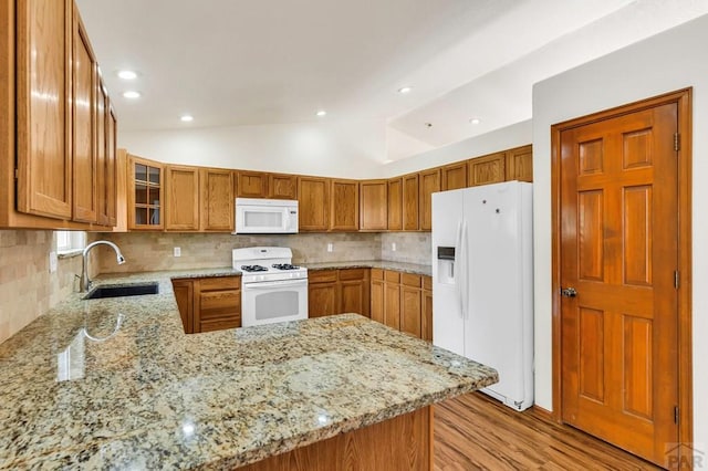 kitchen featuring white appliances, glass insert cabinets, brown cabinets, a peninsula, and a sink