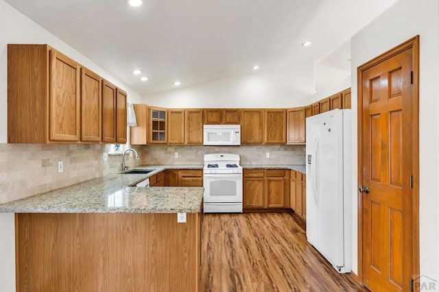 kitchen featuring white appliances, lofted ceiling, glass insert cabinets, a peninsula, and a sink