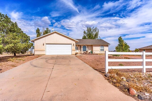 ranch-style home featuring an attached garage, driveway, fence, and stucco siding