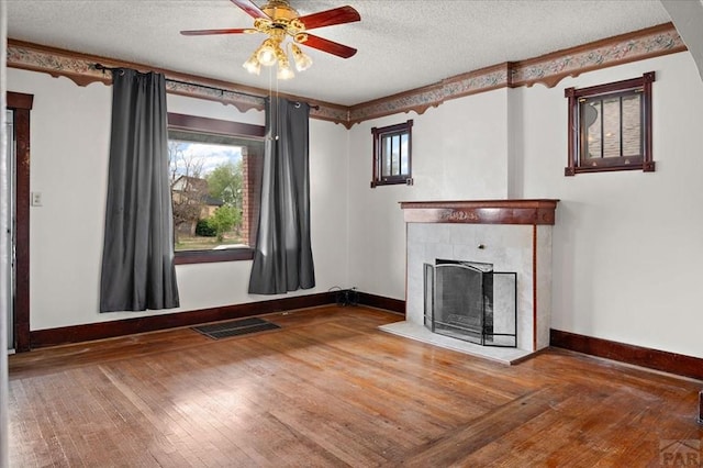 423 Washington St, Pueblo, CO 81004 - unfurnished living room featuring a ceiling fan, wood-type flooring, baseboards, a tiled fireplace, and a textured ceiling