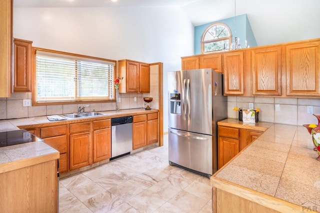 kitchen with tile countertops, stainless steel appliances, a sink, and high vaulted ceiling