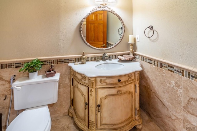 half bath with wainscoting, tile walls, toilet, and vanity