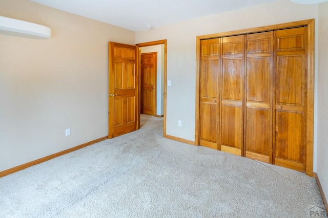 unfurnished bedroom with a closet, an AC wall unit, light colored carpet, and baseboards