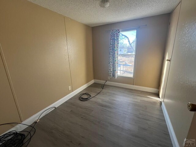 unfurnished room featuring a textured ceiling, baseboards, and wood finished floors