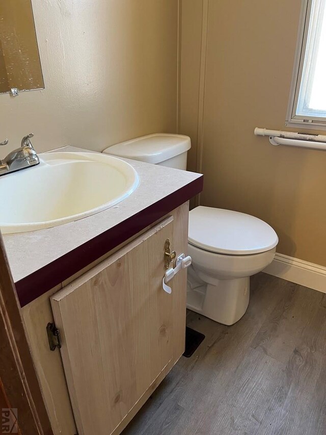 half bath featuring baseboards, vanity, toilet, and wood finished floors