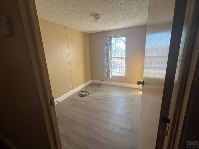 empty room with a textured ceiling, baseboards, and wood finished floors