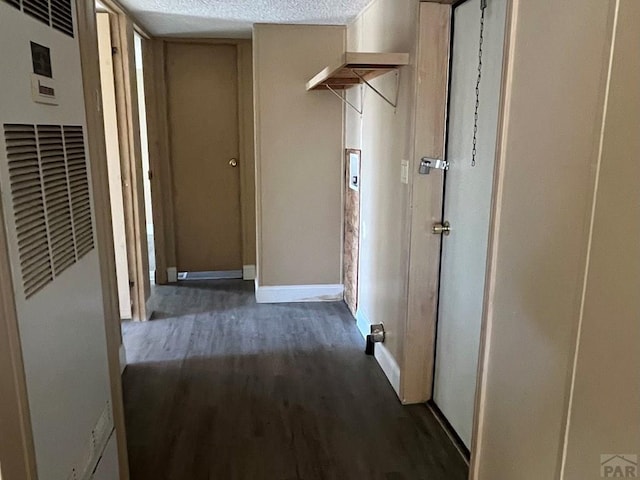 hallway featuring baseboards, a heating unit, dark wood-type flooring, and a textured ceiling