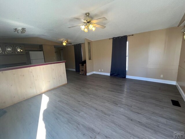 unfurnished living room with baseboards, dark wood finished floors, a ceiling fan, lofted ceiling, and a textured ceiling