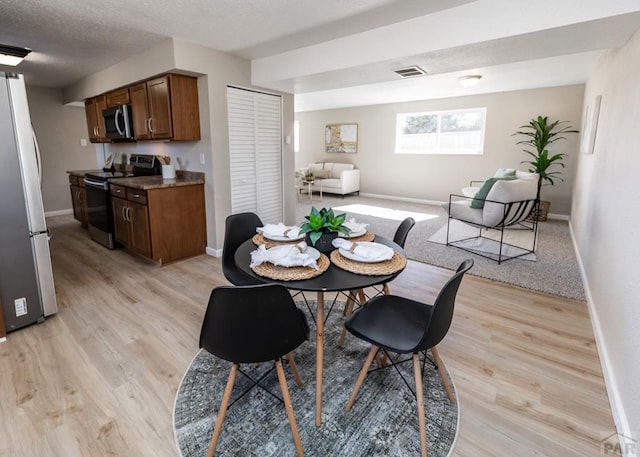 dining area featuring a textured ceiling, baseboards, visible vents, and light wood-style floors