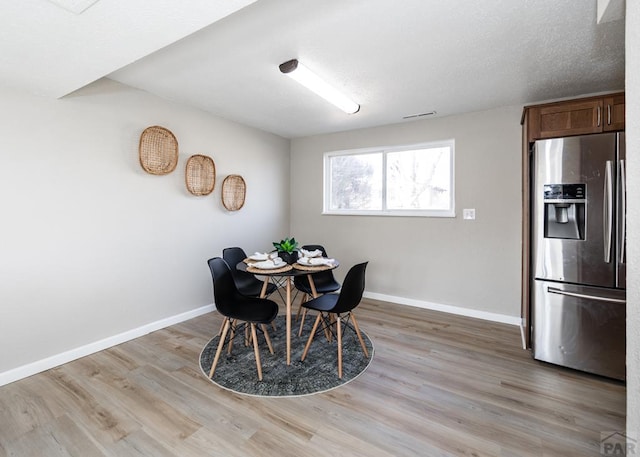 dining area featuring light wood-type flooring, visible vents, baseboards, and a textured ceiling