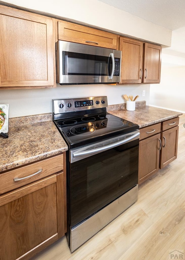 kitchen featuring appliances with stainless steel finishes, light stone countertops, and light wood-style floors